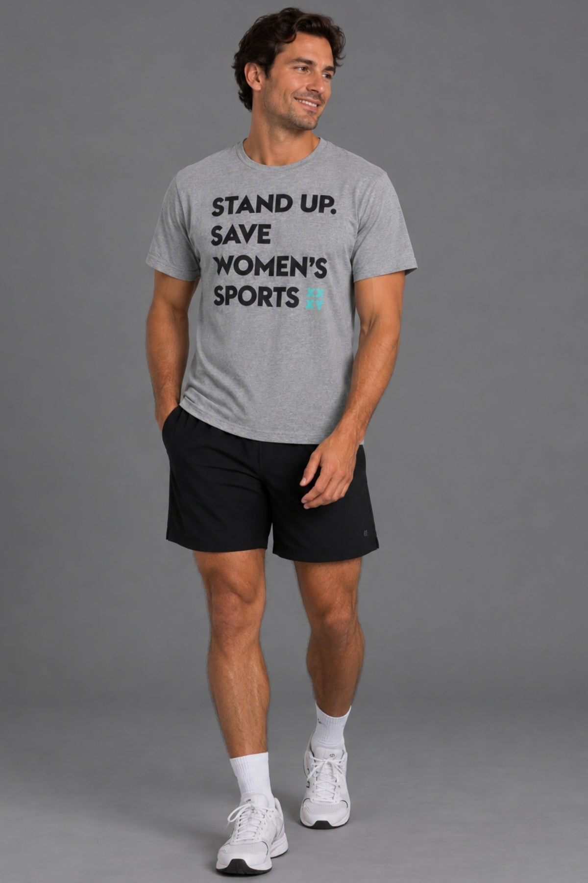 Male model wearing a gray Stand Up. Save Women’s Sports T-shirt, black shorts and white sneakers against a gray background.