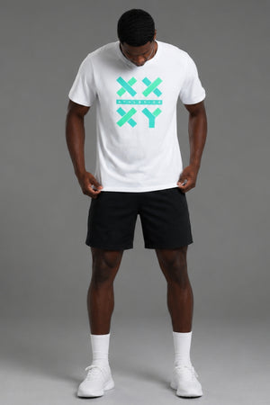 A man wearing a white crewneck t-shirt with a mint green XXYY logo on the chest, paired with black athletic shorts, white socks, and white sneakers, standing against a solid gray studio background. || White