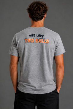 A man viewed from behind wearing a heather gray t-shirt with 'ONE LOVE TWO BALLS' printed on the back in navy and orange, paired with black pants against a solid gray studio background. || Heather Gray