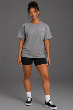 Black female model wearing a boyfriend-fit gray XX-XY Athletics tee with black bike shorts. || Heather Gray