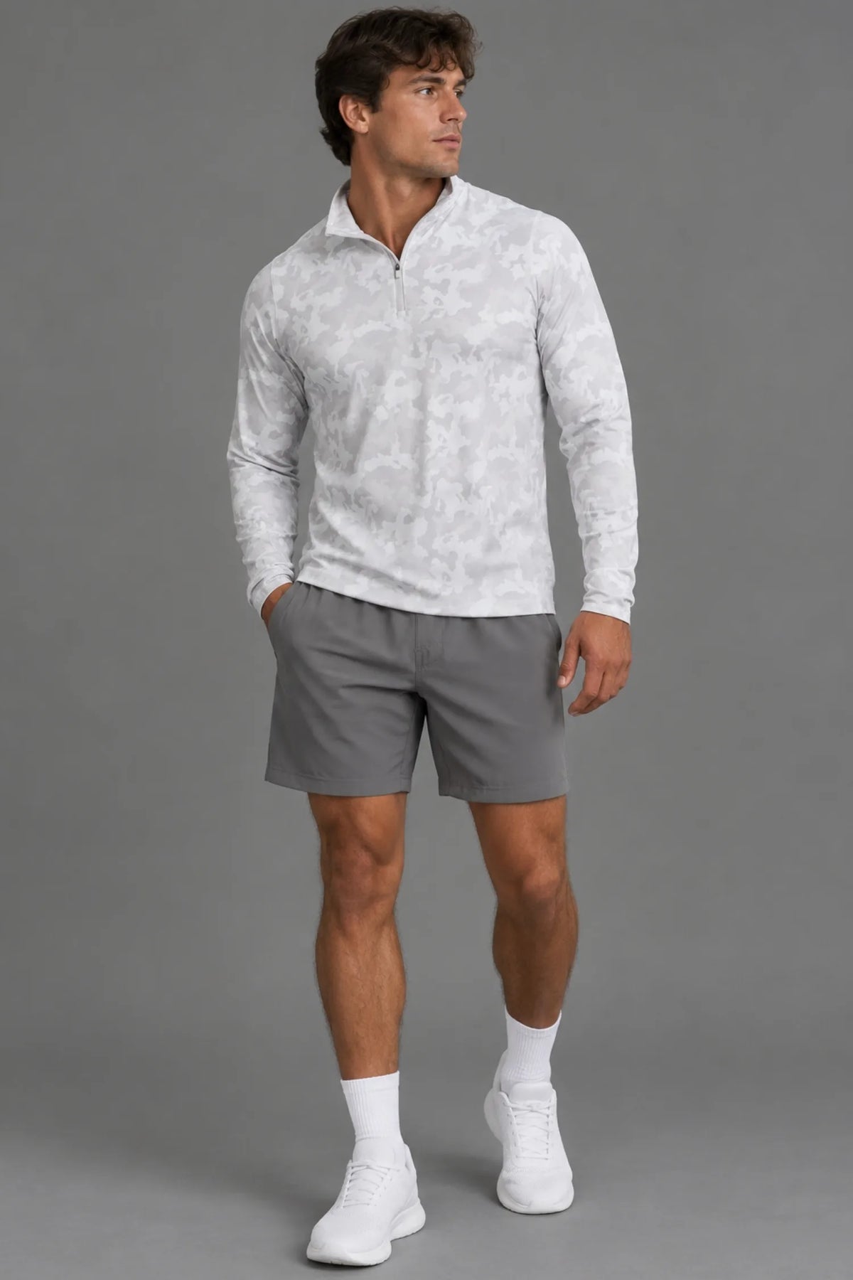 Male model wearing a white camo quarter-zip pullover with gray athletic shorts, white socks, and white sneakers. || White Camo