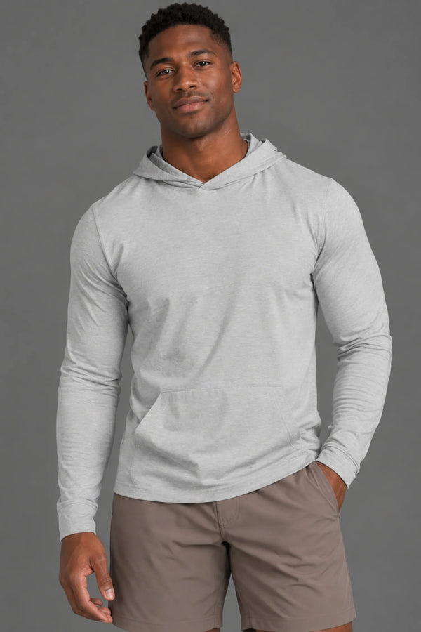 Black male model wearing a light gray performance hoodie and brown athletic shorts with one hand in his pocket. || Light Heather Gray - 1