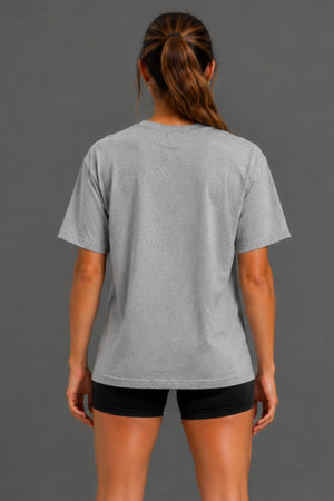 A woman viewed from the back wearing a light gray short-sleeve crewneck t-shirt and black athletic shorts, set against a solid dark gray studio background. || Heather Gray