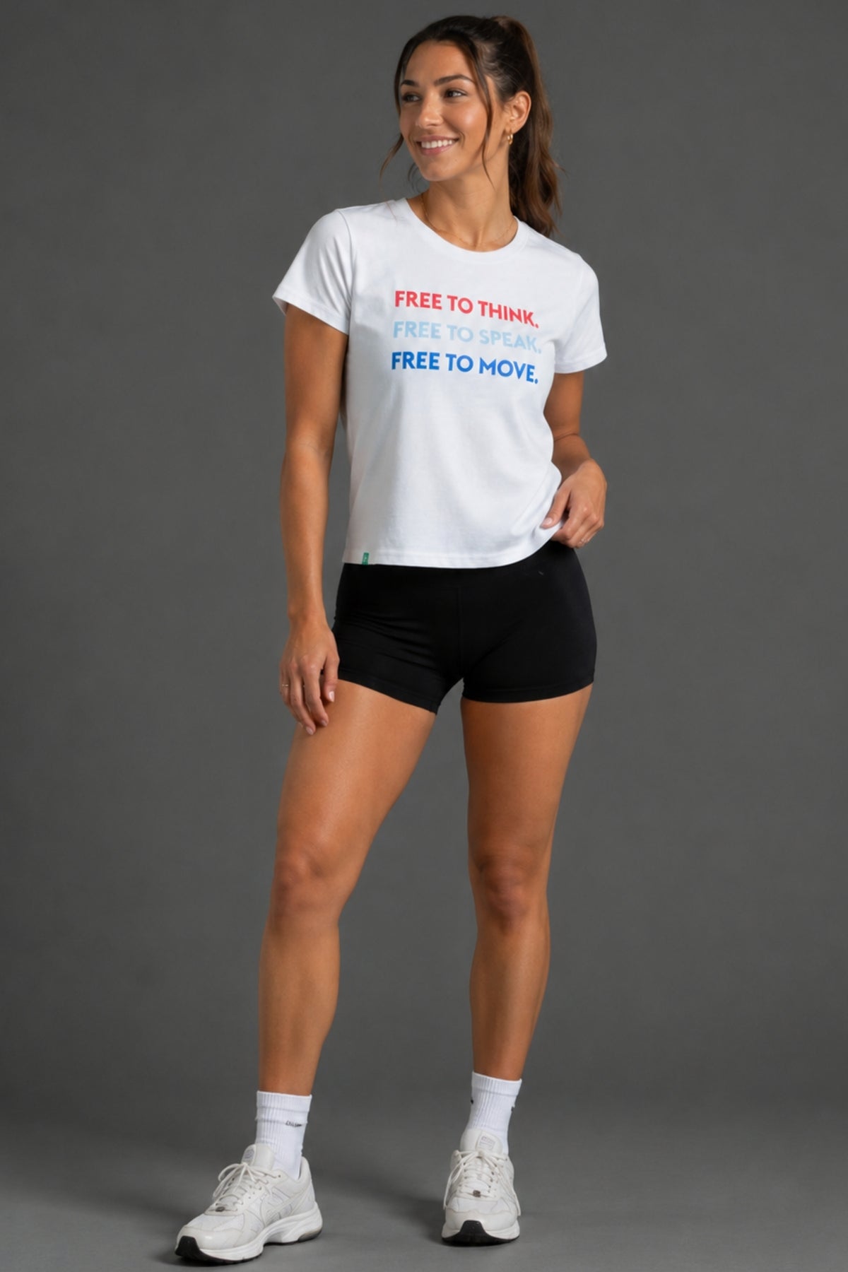 A woman modeling a white graphic t-shirt with red and blue text that reads 'FREE TO THINK. FREE TO MOVE.