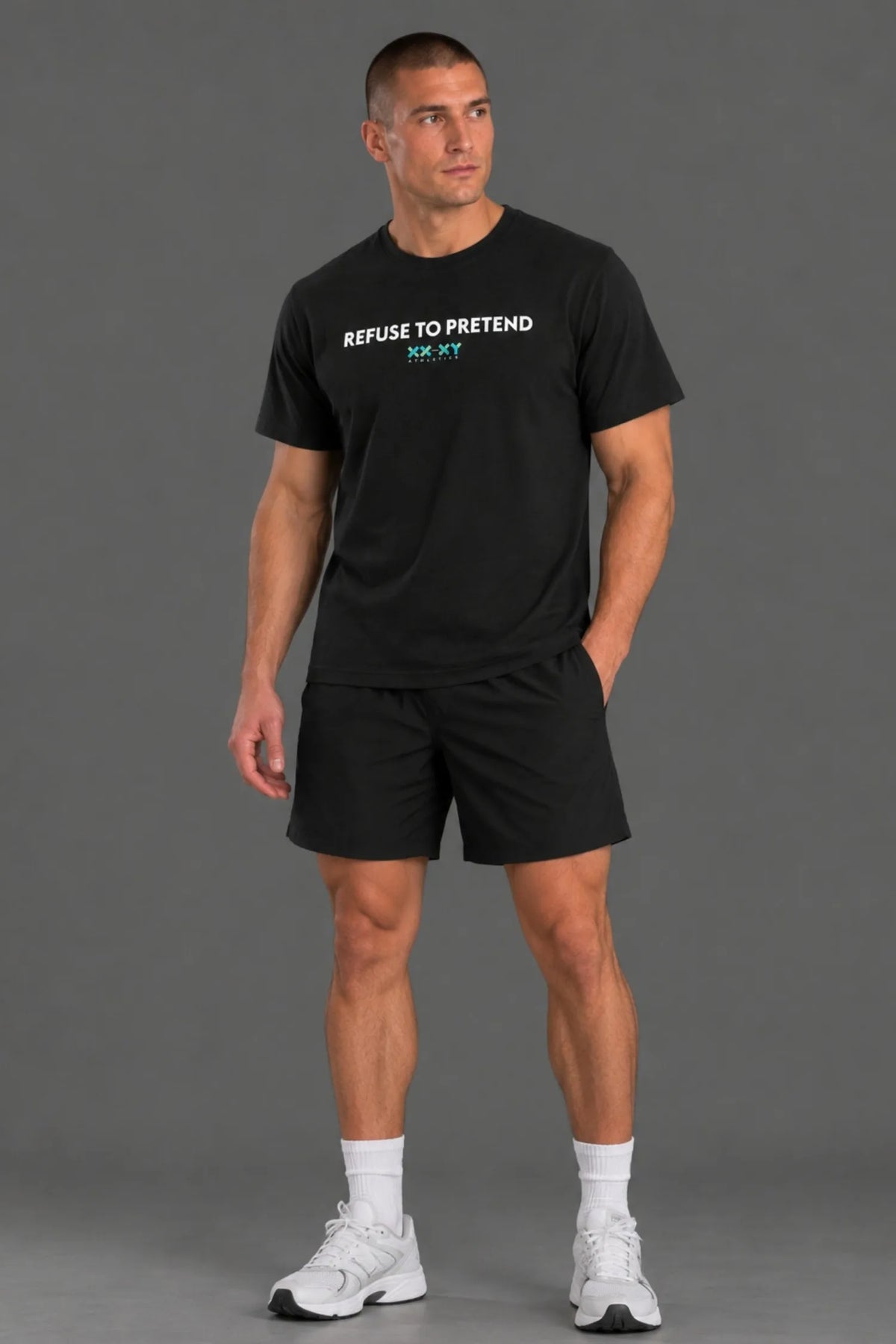 Close-up of a male model wearing a black XX-XY Athletics T-shirt featuring the white "REFUSE TO PRETEND" text and teal logo, with one hand resting behind his neck. || Black