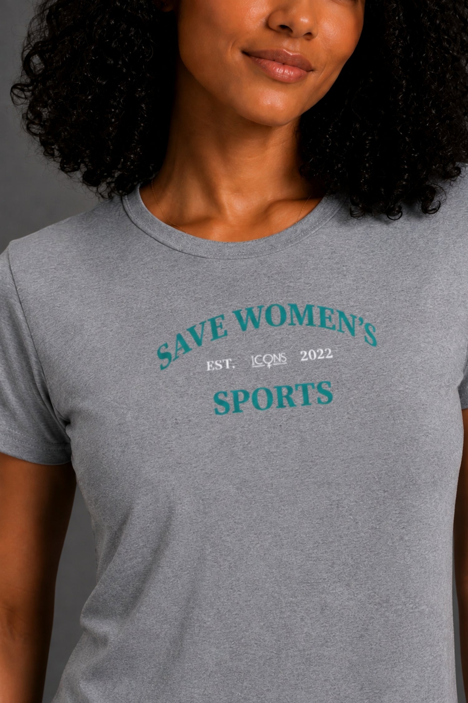 A woman wearing a heather gray crewneck t-shirt with a teal and white graphic that reads 'SAVE WOMEN'S SPORTS EST. 1526 2022'. || Heather Gray