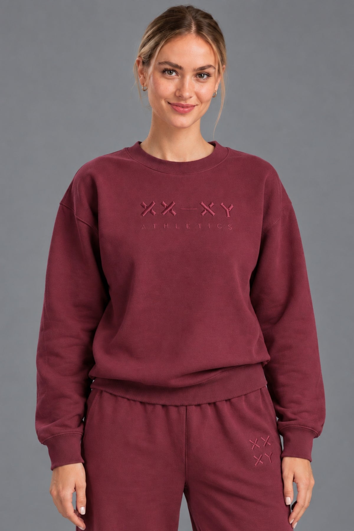 Woman wearing a burgundy XX-XY Athletics crewneck sweatshirt with tonal embroidered logo. || Red Wine