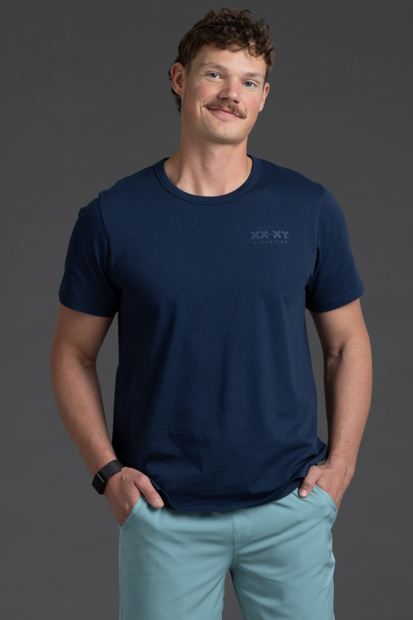 Man wearing a navy blue t-shirt with a logo on a gray background || Navy