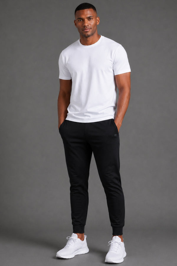 Male model wearing black performance joggers with a white T-shirt and white sneakers on a gray studio background. || Black