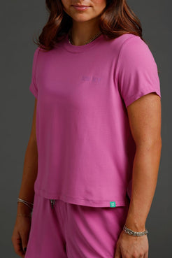 Person wearing a pink t-shirt and pants with a logo on a gray background || Bright Fuchsia