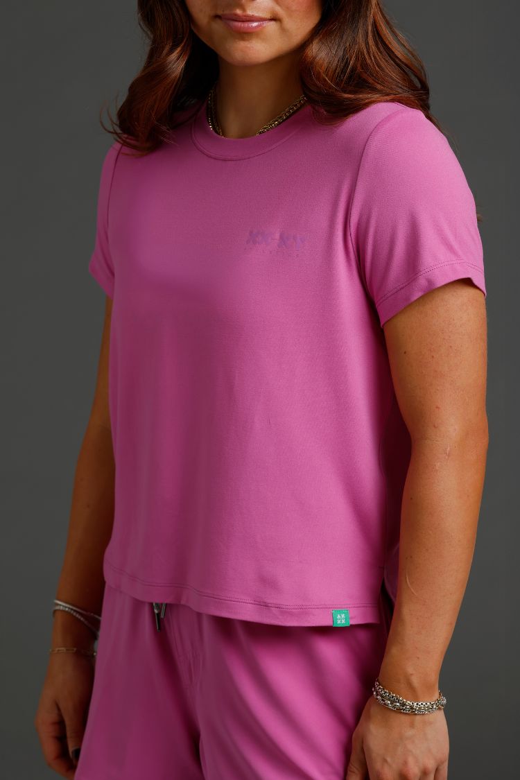 Person wearing a pink t-shirt and pants with a logo on a gray background || Bright Fuchsia