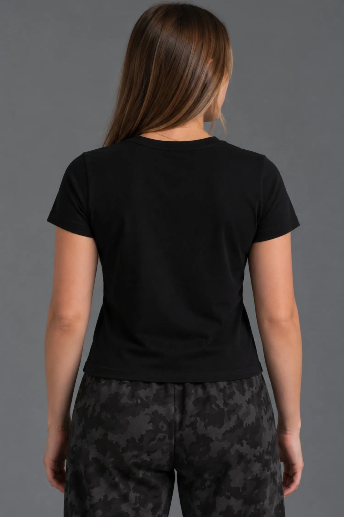 Back view of a female model wearing a blank cropped black tee with black camo sweatpants. || Black