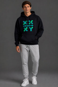 A man modeling a black pullover hoodie with a green and blue geometric 'X' and 'Y' graphic on the chest, paired with light gray sweatpants and white sneakers, against a dark gray studio background. || Black with Color Logo