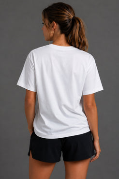 A woman shown from the back wearing a plain white short-sleeve crewneck t-shirt and black athletic shorts against a solid gray studio background. || White