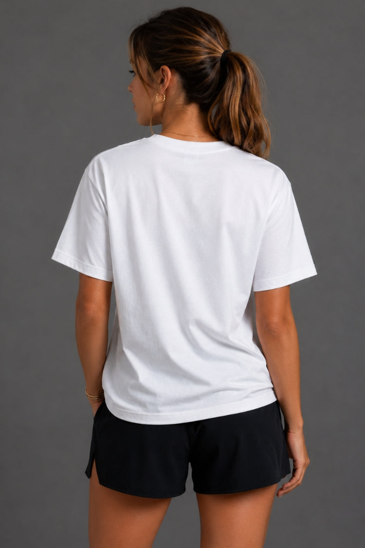A woman shown from the back wearing a plain white short-sleeve crewneck t-shirt and black athletic shorts against a solid gray studio background. || White