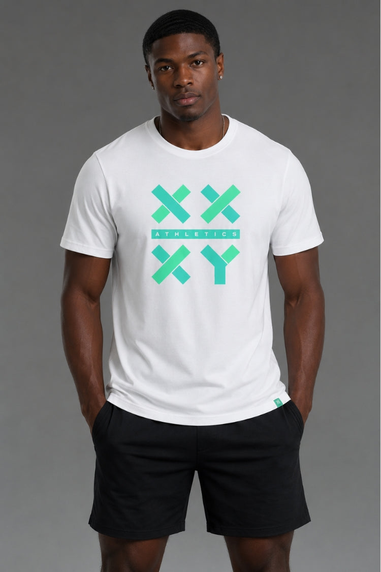 A man wearing a white crewneck t-shirt with a green and teal graphic on the chest that reads 'XX ATHLETICS XY' and black athletic shorts, standing against a solid gray studio background. || White