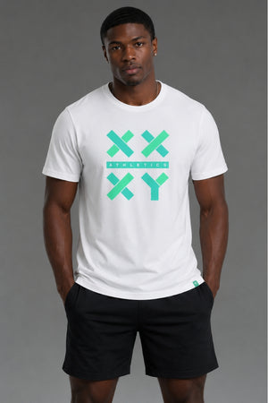 A man wearing a white crewneck t-shirt with a green and teal graphic on the chest that reads 'XX ATHLETICS XY' and black athletic shorts, standing against a solid gray studio background. || White