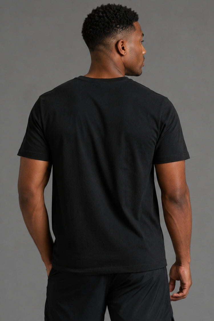 A man viewed from the back wearing a plain black short-sleeve crew-neck t-shirt and black pants, set against a solid gray studio background. || Black