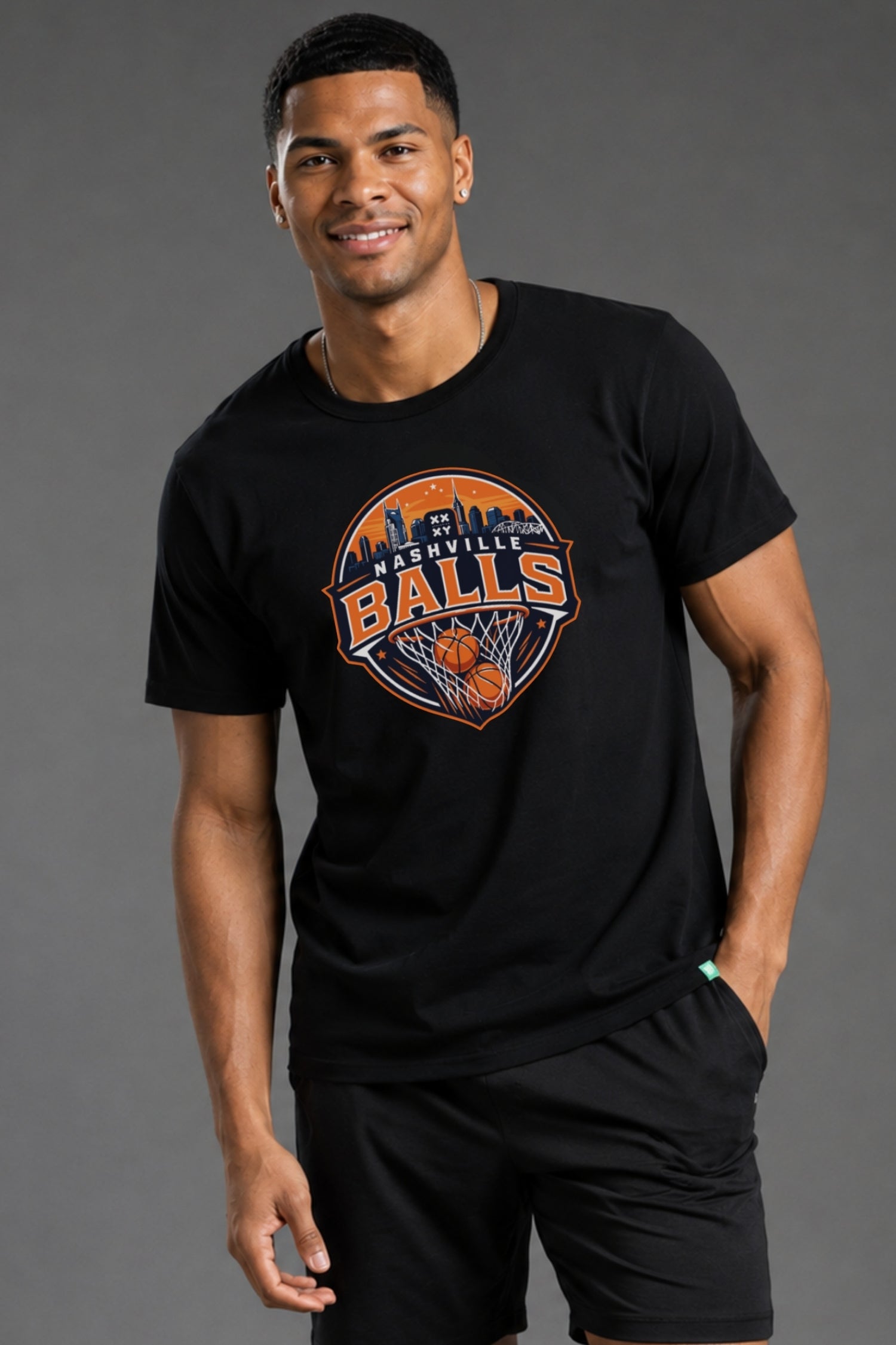 A man wearing a black crewneck t-shirt with a circular 'Washington Ballers' basketball graphic on the chest, paired with black athletic shorts, against a solid gray studio background. || Black