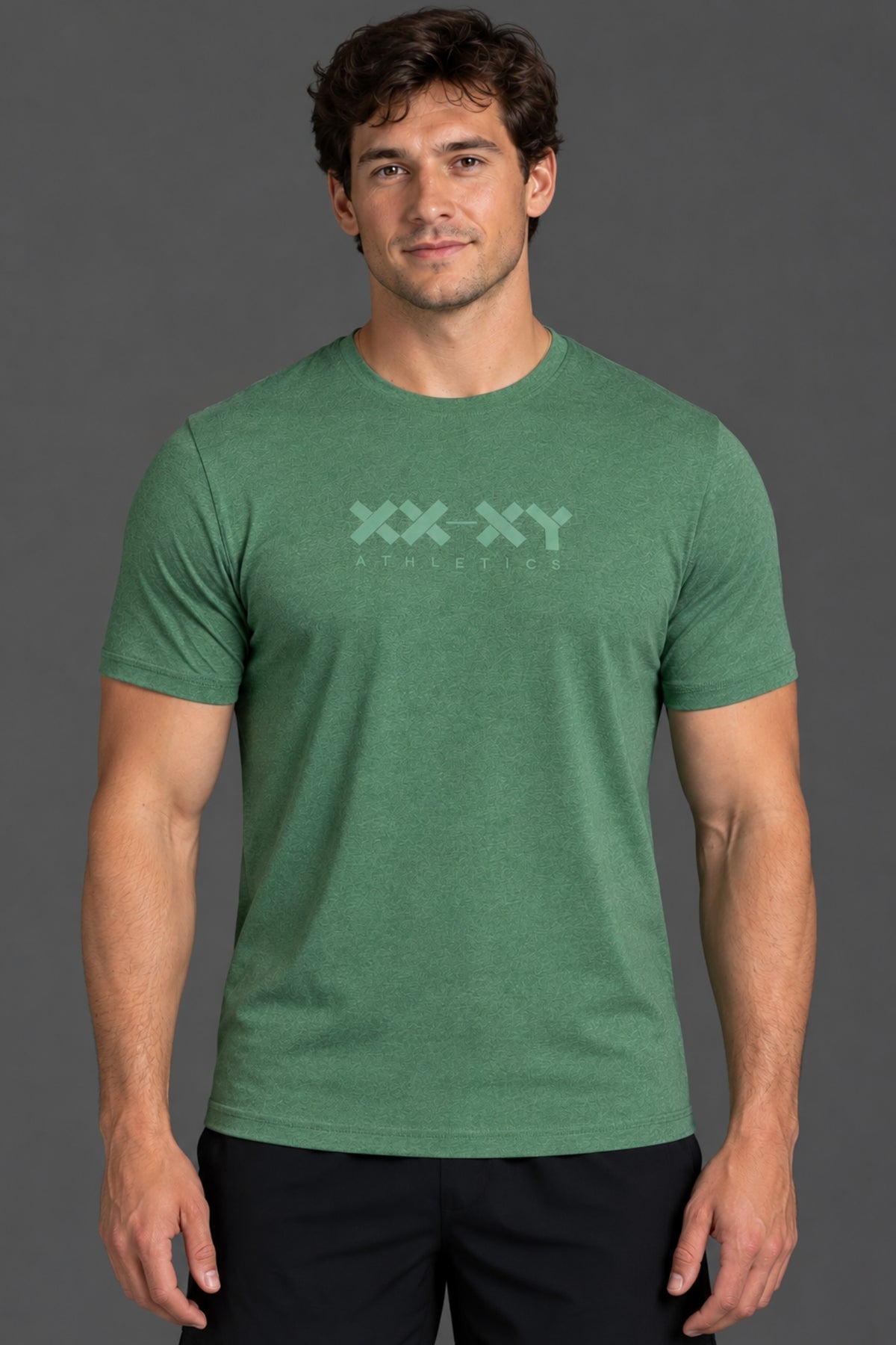 A man wearing a heather green crewneck t-shirt with a light green 'XX-XY AESTHETICS' logo printed across the chest, set against a solid dark gray studio background.