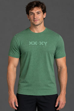 A man wearing a heather green crewneck t-shirt with a light green 'XX-XY AESTHETICS' logo printed across the chest, set against a solid dark gray studio background. || Hunter Green Heather