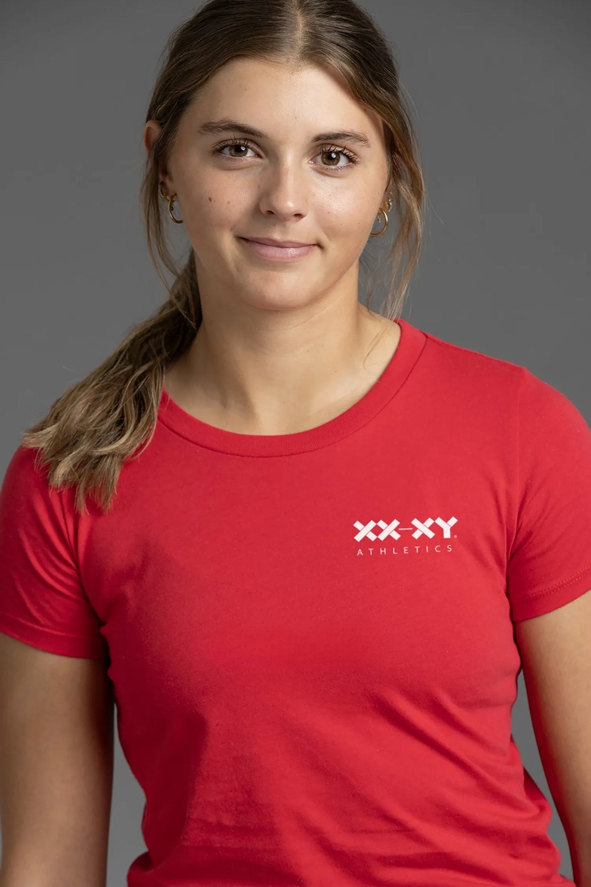 Close-up of a female model wearing a red XX-XY Athletics T-shirt, highlighting the white XX-XY Athletics chest logo, crew neckline, and soft cotton fabric.