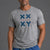 A man wearing a heather gray athletic t-shirt with a blue 'XXY' logo and 'ATHLETICS' text on the chest, paired with blue drawstring sweatpants, against a solid gray studio background. || Gray Camo