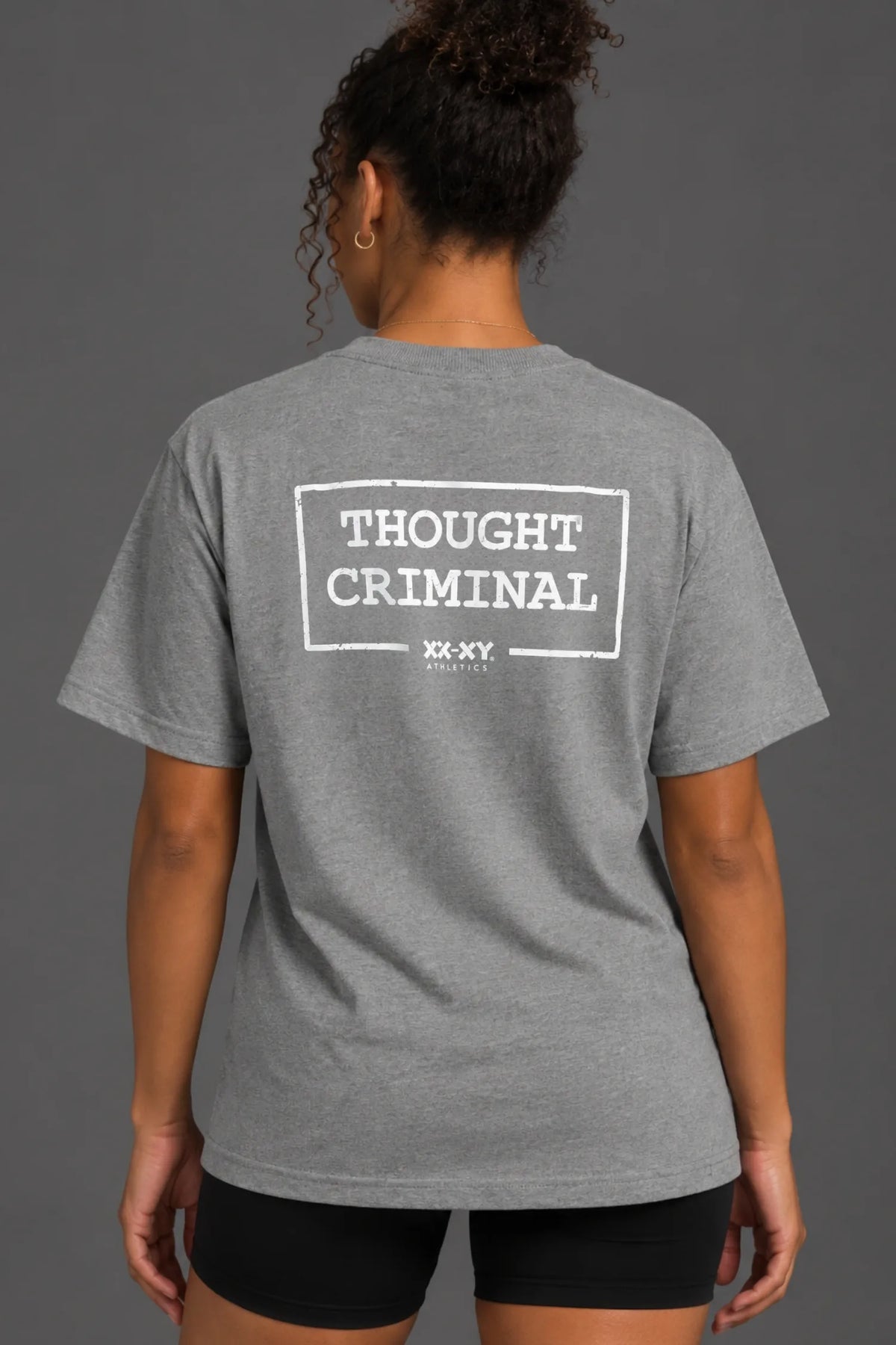 Black female model wearing a boyfriend-fit gray Thought Criminal graphic tee with black bike shorts.
