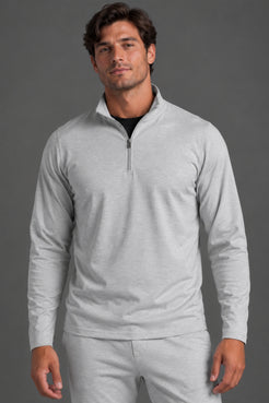 A man wearing a light gray heathered quarter-zip long-sleeve pullover and matching sweatpants, photographed against a solid dark gray studio background. || Light Heather Gray - 1