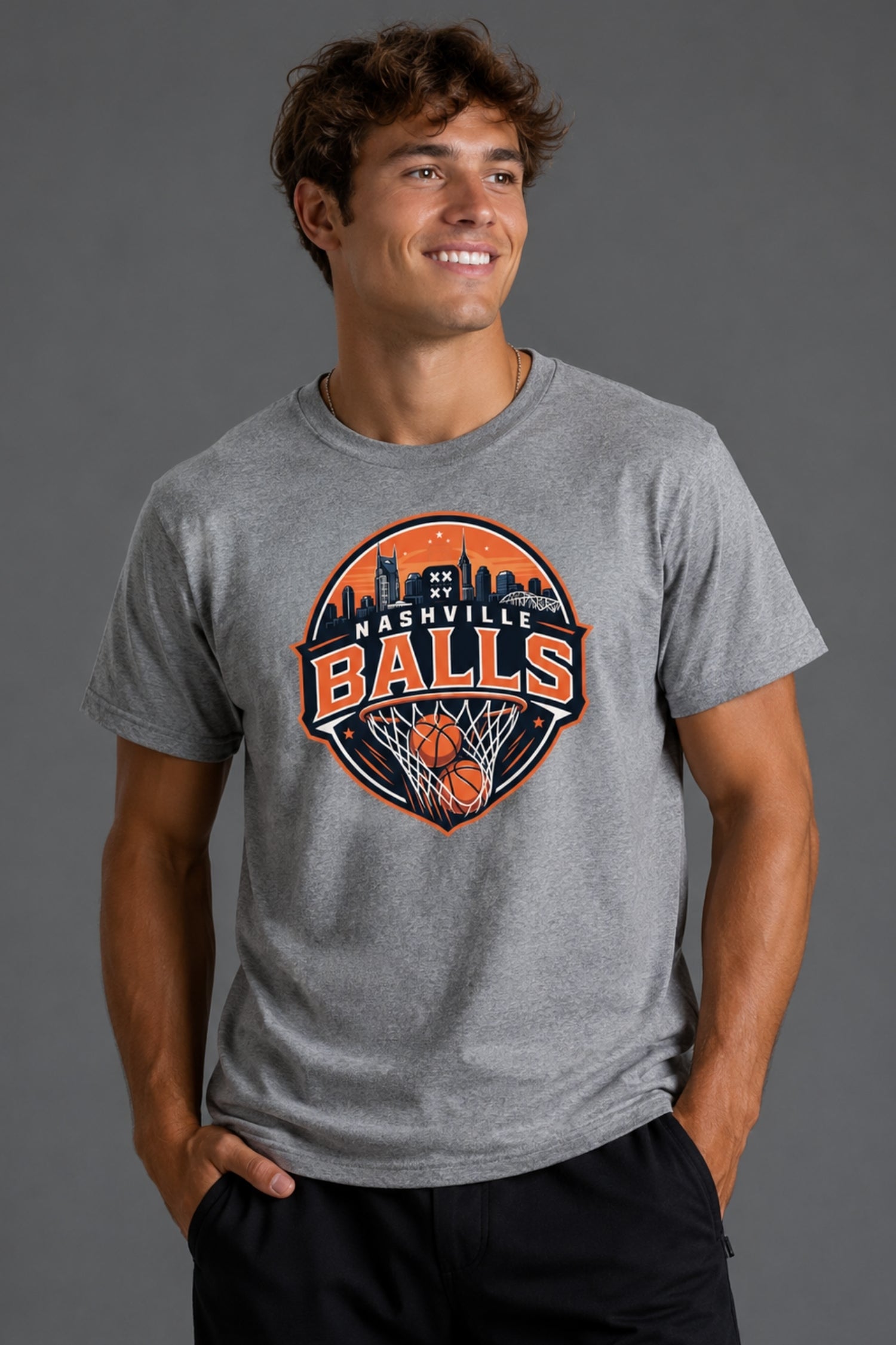 A man modeling a heather gray t-shirt with a 'Falcon Bats' graphic on the chest, paired with black athletic shorts, white socks, and white sneakers against a solid gray studio background. || Heather Gray