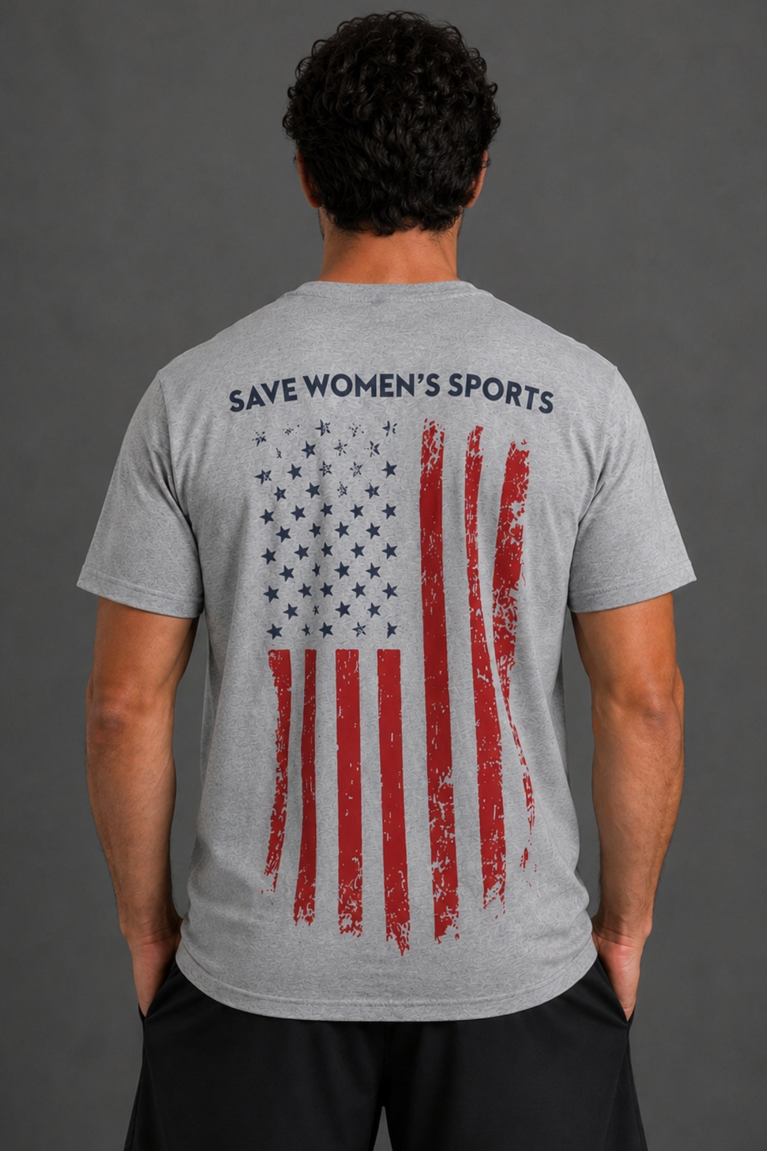 A man viewed from behind wearing a heather gray t-shirt with a distressed American flag graphic and the text 'SAVE WOMEN'S SPORTS' printed across the upper back.