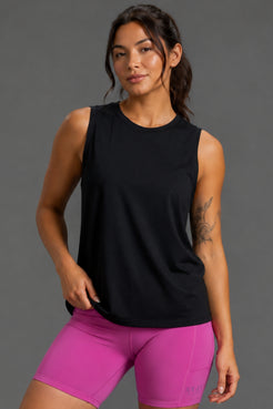 A woman modeling a sleeveless black athletic tank top paired with bright pink fitted shorts against a plain gray studio background. || Black