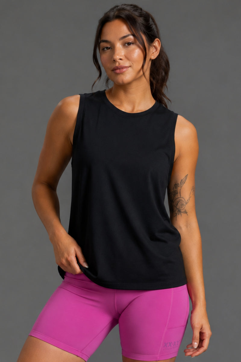 A woman modeling a sleeveless black athletic tank top paired with bright pink fitted shorts against a plain gray studio background. || Black
