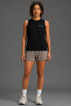 A woman modeling a sleeveless black athletic tank top with a small teal logo on the chest, paired with taupe athletic shorts, white socks, and white sneakers, against a solid gray studio background. || Black