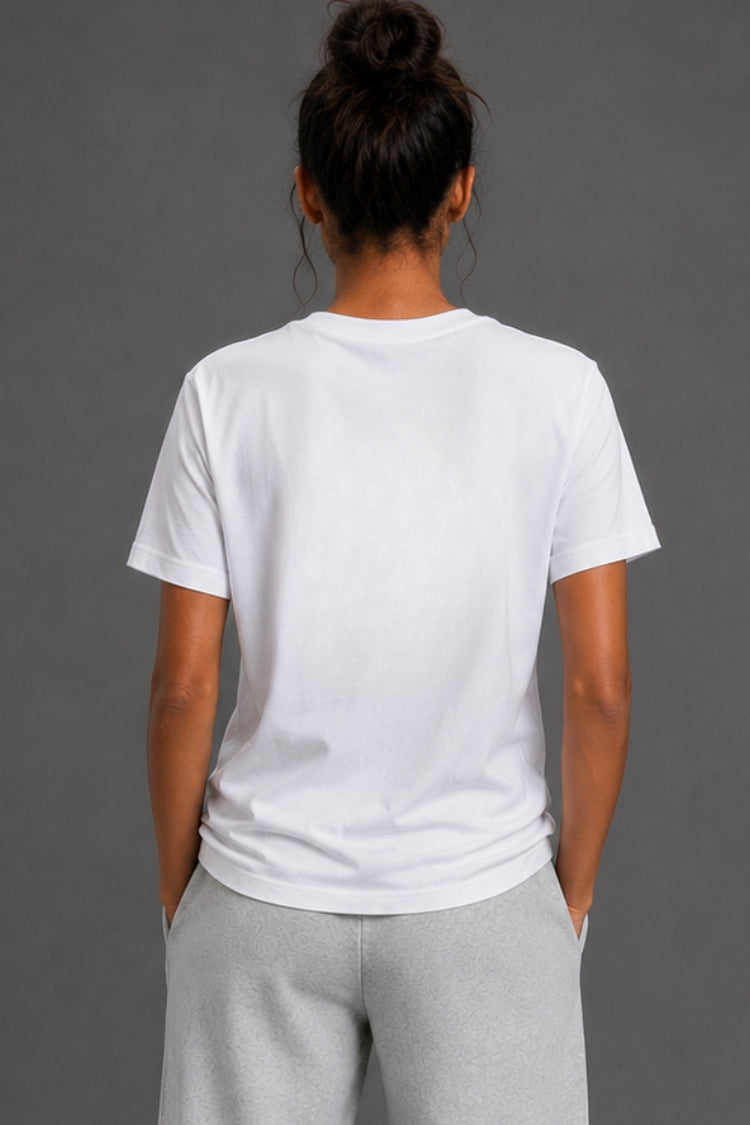A woman viewed from behind wearing a plain white short-sleeve crewneck T-shirt and light gray sweatpants against a solid dark gray studio background.