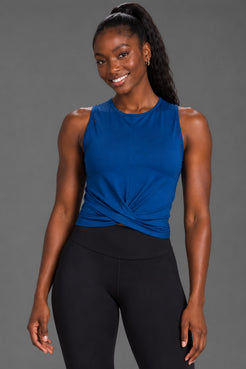 Black female model wearing a blue twist-front tank and black XX-XY Athletics leggings on a gray studio background. || Navy