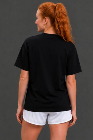 A woman with red hair in a ponytail is shown from the back, wearing a plain black short-sleeve t-shirt and white athletic shorts against a dark gray studio background. || Black