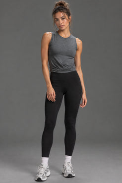 Female model wearing a dark heather gray twist-front tank top and black leggings, standing against a gray studio background. || Dark Heather Gray