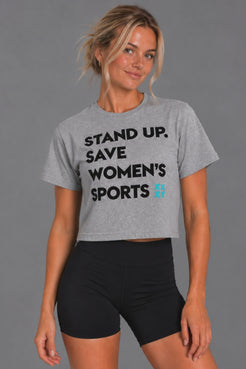 Blonde woman wearing the gray cropped Stand Up Save Women’s Sports tee with black bike shorts || Heather Gray