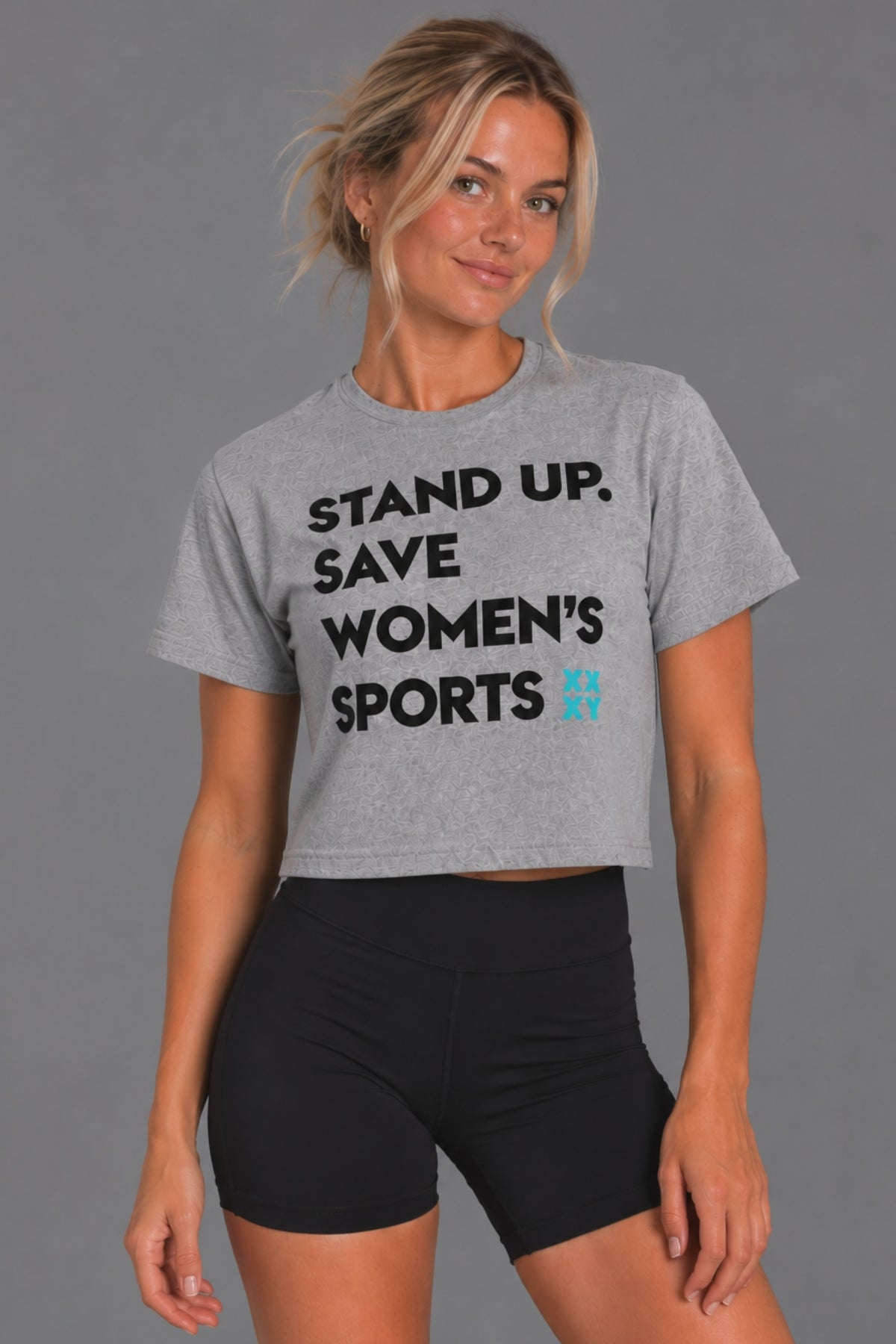 Blonde woman wearing the gray cropped Stand Up Save Women’s Sports tee with black bike shorts || Heather Gray