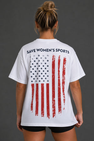 A woman viewed from the back wearing a white graphic T-shirt with the text 'SAVE WOMEN'S SPORTS' above a distressed American flag design in red, white, and blue. She is also wearing black shorts against a dark gray studio background. || White