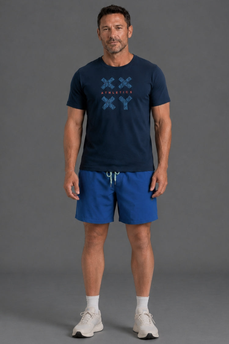 A man modeling a navy blue t-shirt with a blue graphic print and matching blue athletic shorts, standing against a solid gray studio background.