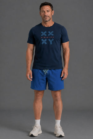 A man modeling a navy blue t-shirt with a blue graphic print and matching blue athletic shorts, standing against a solid gray studio background. || Navy Camo