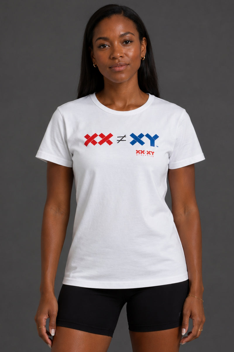 A woman modeling a white short-sleeve crewneck t-shirt with a red and blue chest graphic reading 'XX ≠ ♦ XY' and 'XX-XY' underneath, paired with black bike shorts against a dark gray studio background. || White