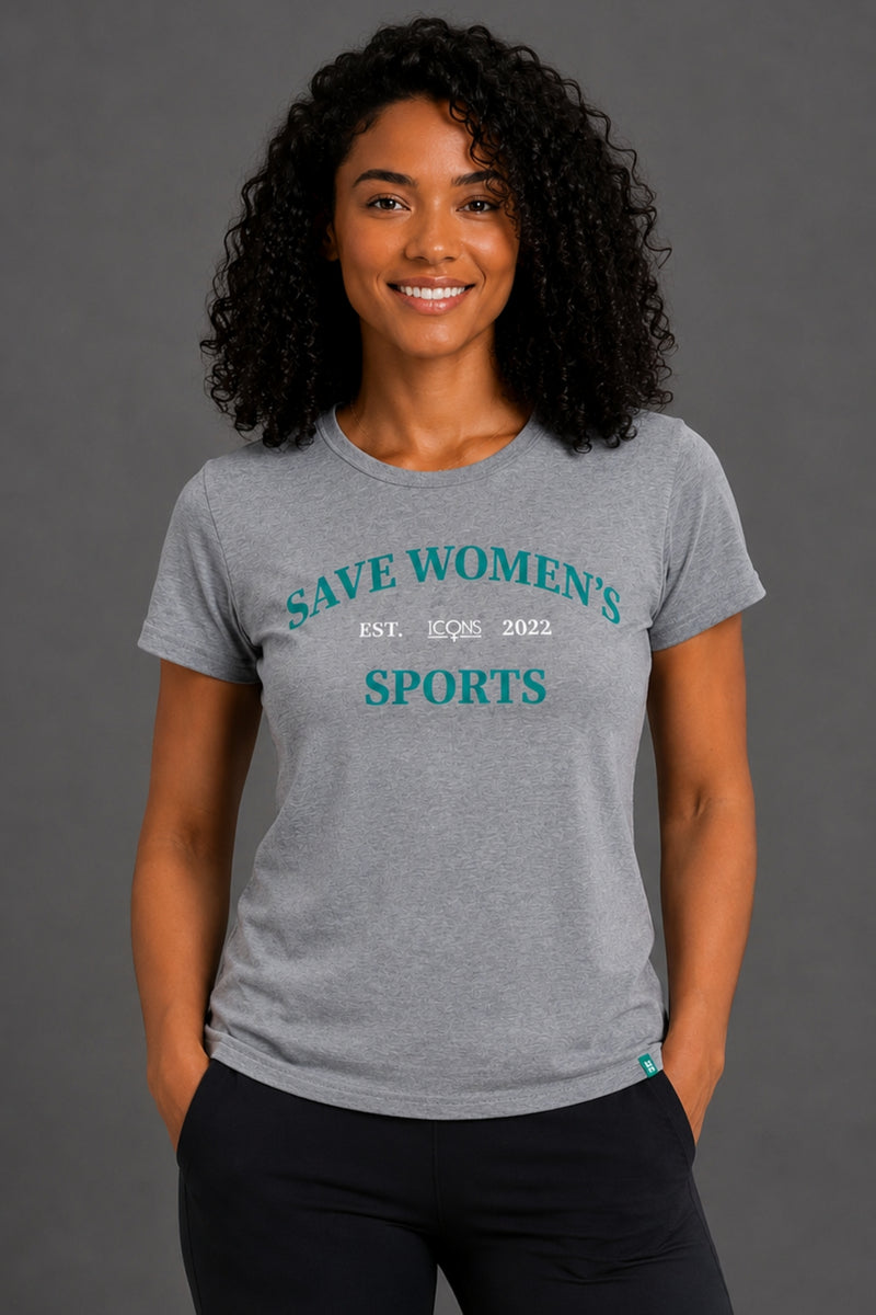 A smiling woman with curly black hair wearing a heather gray graphic t-shirt with teal text reading 'SAVE WOMEN'S SPORTS' and black pants, standing against a solid gray studio background. || Heather Gray