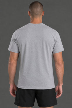 A man viewed from behind wearing a light gray heather crewneck t-shirt and black athletic shorts, standing against a solid dark gray studio background. || Light Heather Gray