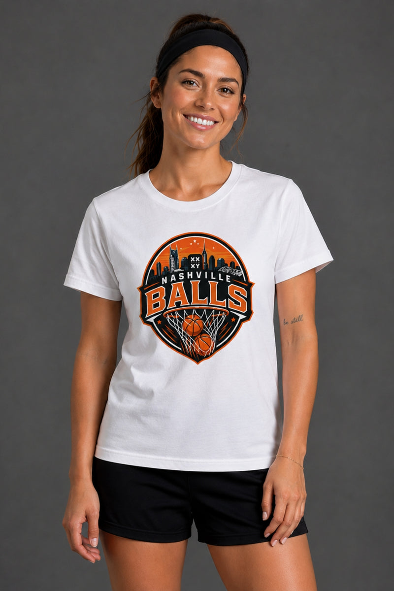 A woman wearing a white short-sleeve graphic T-shirt with a circular 'Nashville Balls' basketball logo on the front, paired with black athletic shorts, against a dark gray studio background. || White