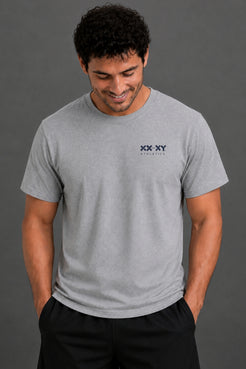 A man wearing a light gray crewneck t-shirt with a small black 'XX-XY' logo on the left chest, paired with black pants, set against a solid dark gray background. || Heather Gray