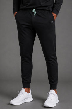 Front view of men’s black tapered joggers styled with a white T-shirt and white athletic sneakers. || Black