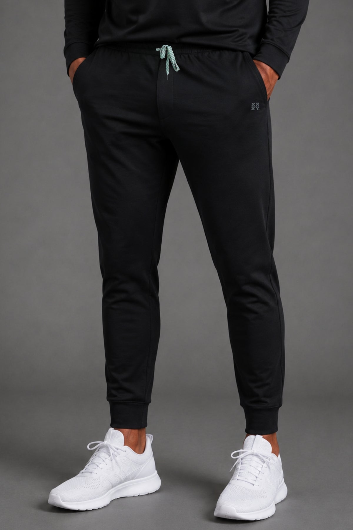 Front view of men’s black tapered joggers styled with a white T-shirt and white athletic sneakers. || Black